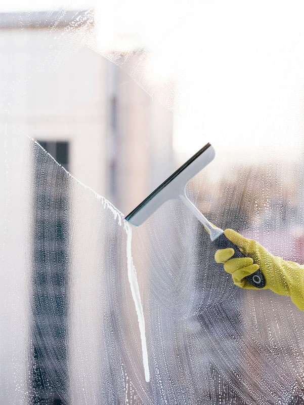 Eine Person mit einem gelben Handschuh reinigt fachmännisch und streifenfrei ein Fenster mit einem Abzieher und verkörpert so die Qualität der Fensterreinigung Graz.