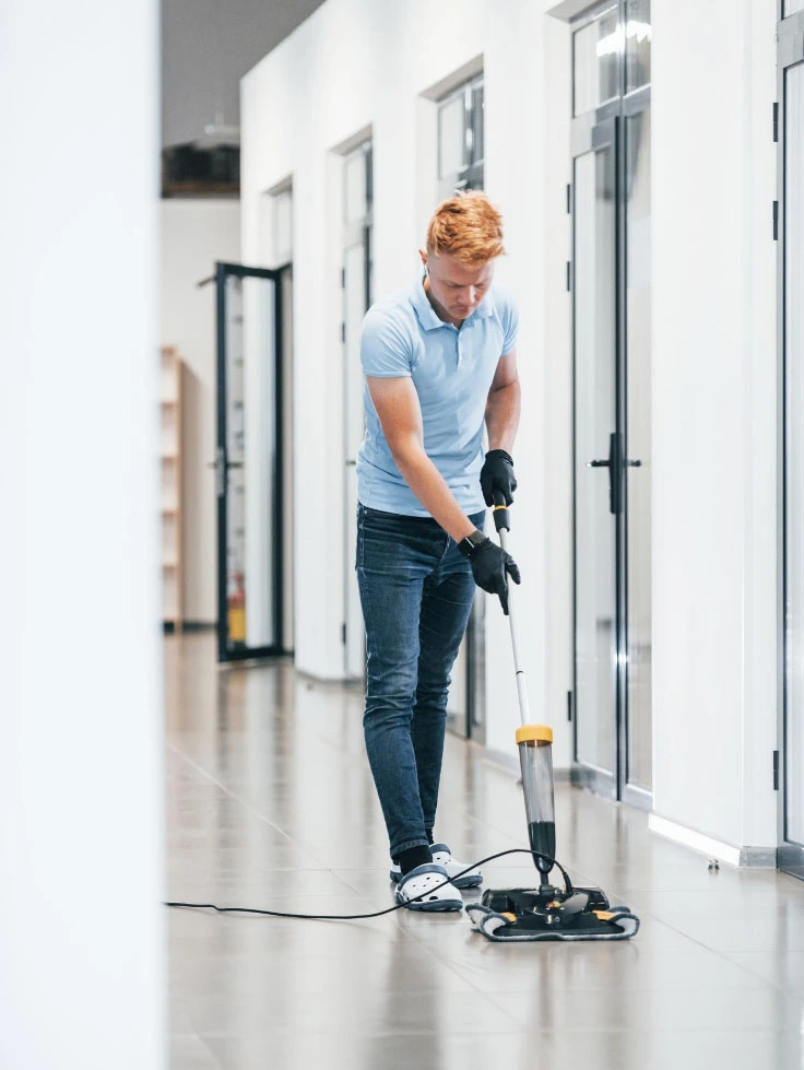 Eine Person in blauem Hemd und Jeans bedient eine Bodenreinigungsmaschine und pflegt den Flur fachmännisch im Rahmen des erstklassigen Services der Hausbetreuung Graz.